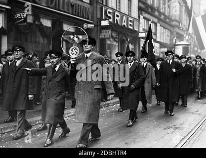 Après le référendum sur l'annexion de la Sarre au Reich allemand, les hommes marchent dans les rues de Saarbruecken avec les drapeaux de la croix gammée et les symboles souverains du Reich. Banque D'Images