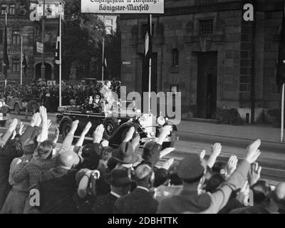 « Adolf Hitler, en Mercedes, avec Julius Schaub assis derrière lui, est accueilli par les gens enthousiastes de Nuremberg et conduit à l'hôtel Deutscher Hof, où il sera resté pendant le Congrès du Parti nazi à Nuremberg. Ci-dessus se trouve un panneau avec l'inscription ''point d'embarquement en direction: Koenigstor-Maxfeld''.' Banque D'Images