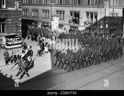 Les membres du Reich Labour Service marchent derrière leur drapeau avec des bêches entre leurs mains dans leurs quartiers sur le site du rassemblement du parti nazi. Au bord de la route, ils sont accueillis par la population. Sur la gauche se trouve un stand de fruits décoré du drapeau de Reich et de swastikas. Banque D'Images