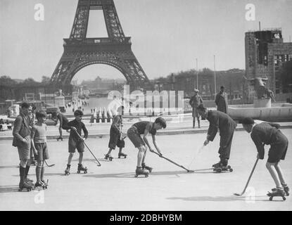 Certains garçons jouent au hockey sur gazon sur patins à roulettes sur la place du Trocadéro en face de la Tour Eiffel à Paris. Sur la droite se trouve la fontaine du Trocadéro, qui a une statue d'un taureau au milieu. Banque D'Images