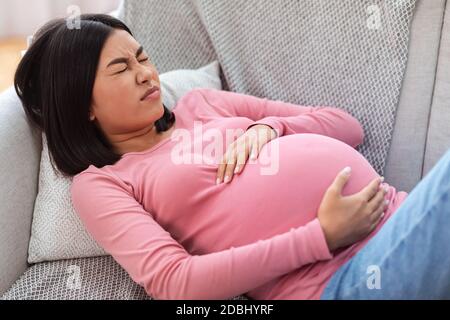 Femme chinoise enceinte souffrant de douleurs touchant Belly à la maison Banque D'Images