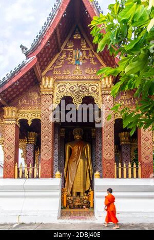 Un jeune moine bouddhiste se dresse devant une grande statue de Bouddha d'or à Luang Prabang, Laos, Indochine, Asie du Sud-est, Asie Banque D'Images