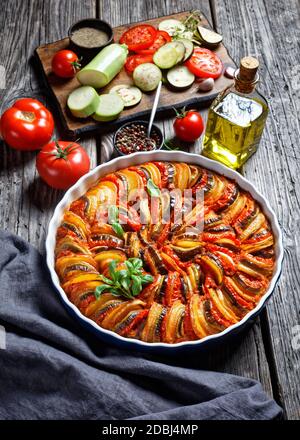 ratatouille, ragoût de légumes en tranches d'aubergines, courgettes, oignons et pommes de terre avec sauce tomate, ingrédients à l'arrière-plan, cuisine française, verticale Banque D'Images