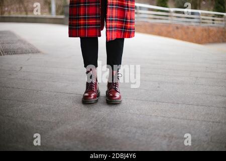 Taille basse portant des bottes rouges tendance et un fond de trench gris Banque D'Images