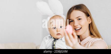 Maman et bébé avec des oreilles de lapin, avec des œufs de Pâques dans leurs mains, assis sur le canapé, parents et enfants jouent à l'intérieur. La famille fête Pâques Banque D'Images