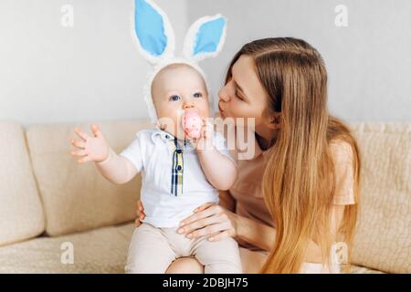 Maman et bébé avec des oreilles de lapin, avec des œufs de Pâques dans leurs mains, assis sur le canapé, parents et enfants jouent à l'intérieur. La famille fête Pâques Banque D'Images