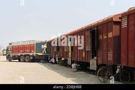 Les travailleurs manuels déplacent de lourds sacs de ciment du train chargé au camion d'attente dans des conditions chaudes et poussiéreuses à Mathura, Uttar Pradesh, Inde. Banque D'Images