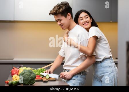 Femme japonaise embrassant mari pendant qu'il cuisine dîner dans la cuisine Banque D'Images