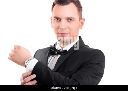 Portrait d'un jeune homme confiant et attrayant en costume noir avec noeud papillon, en ajustant les boutons de manchette sur sa chemise blanche, en regardant l'appareil photo, isolé o Banque D'Images