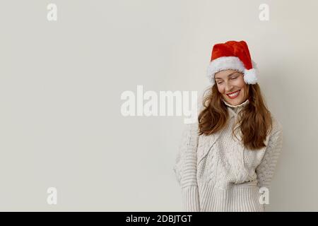 Femme portant un chandail et un chapeau de père noël regardant vers le bas et souriant Banque D'Images