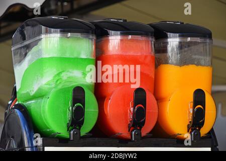 Gros plan sur les glaçons à la glace rouge, orange et vert, les boissons fouettées Granita dans les boîtes de la machine, vue latérale à angle bas Banque D'Images