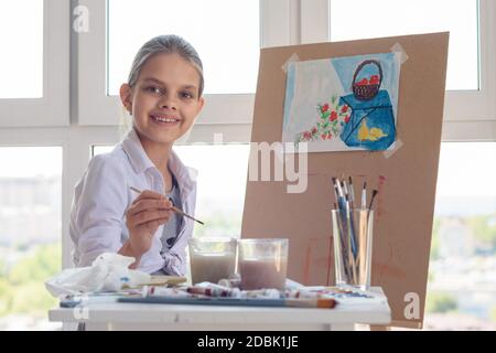 Une fille souriante s'assoit au travail en studio avec une brosse dans ses mains Banque D'Images