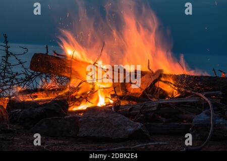 Feu de camp au crépuscule sur la plage. Gros plan sur le feu avec des étincelles et une onde de chaleur. Banque D'Images