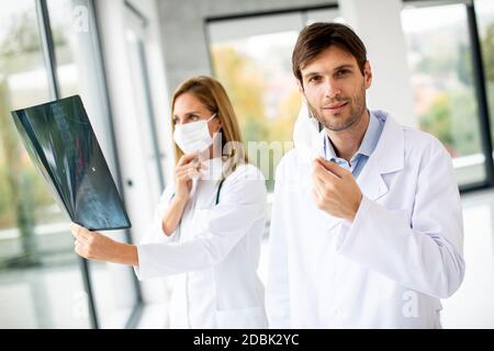 Équipe de médecins examinant la radiographie pendant que le médecin de sexe masculin prend son congé son masque facial de protection dans le bureau médical Banque D'Images