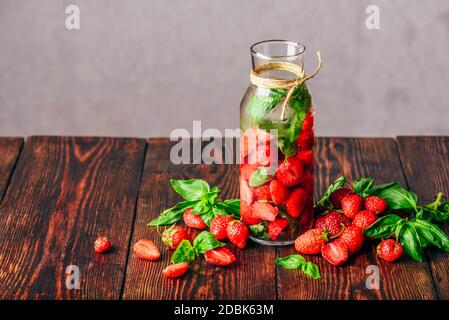 L'eau aromatisée en bouteille avec des fraises fraîches et de feuilles de basilic. Ingrédients éparpillés sur la table en bois. Copier l'espace. Banque D'Images