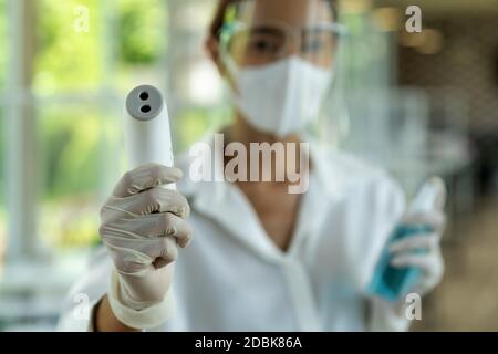 Portrait attrayant serveuse asiatique porter un masque et un masque facial tenir le thermomètre et l'assainisseur de gel d'alcool pour le nettoyage et l'hygiène avec le repos intérieur Banque D'Images