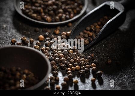 Grains de poivre noir dans une pelle en bois noir sur fond sombre Banque D'Images