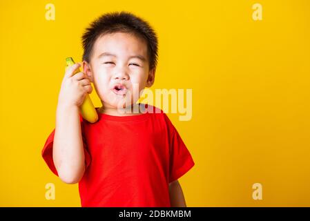 Joyeux portrait enfant ou enfant asiatique mignon petit garçon beau sourire portant un t-shirt rouge jouant tient banane fruit prétendant être comme un téléphone, s Banque D'Images