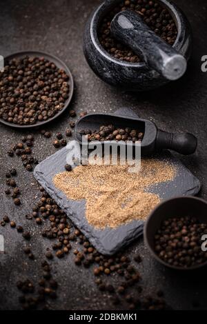 Cornes de poivre noir et poudre de poivre noir sur fond sombre Banque D'Images