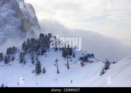 Remontée mécanique md skieurs descendant une pente bosselée avec le Sassolungo derrière, dans la soirée, Val Gardena, Dolomites, Italie. Banque D'Images