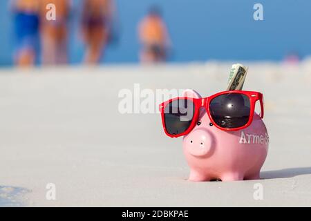 Moneybox de porc rose en lunettes de soleil rouges sur la plage Banque D'Images