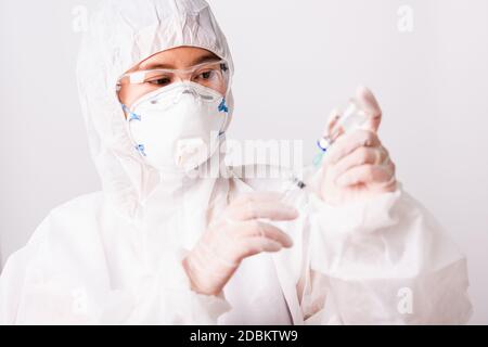 Gros plan de la main de médecin ou scientifique de femme dans la suite EPI uniforme porter masque de protection en laboratoire tenir médicament liquide vaccin flacon et syring Banque D'Images