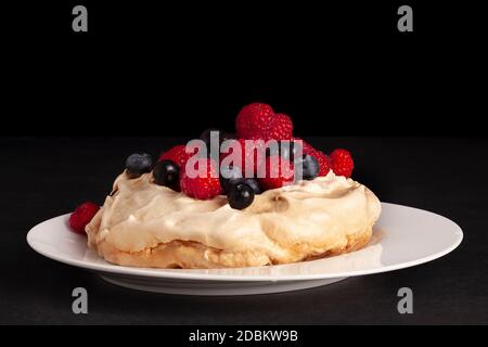 Dessert meringue Pavlova avec baies fraîches et framboises sur fond noir. Banque D'Images