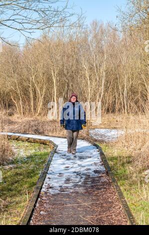 Femme marchant sur une passerelle d'observation des oiseaux au RSPB Dungeness pendant l'hiver. Banque D'Images