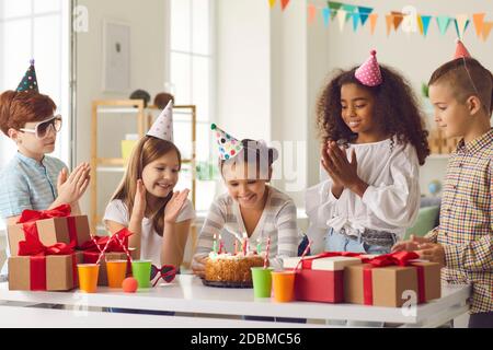 Bonne fille faisant son souhait d'anniversaire avant de souffler des bougies sur gâteau pendant la fête avec des amis Banque D'Images