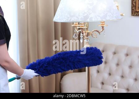 La femme de ménage dépoussiérez le lampadaire à l'aide d'une grande brosse. Une photo méconnaissable . Concept de nettoyage dans un hôtel ou à la maison. Copier l'espace. Banque D'Images