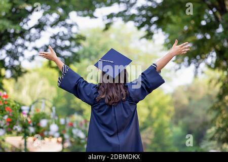 La vue arrière de la jeune femme qui obtient son diplôme lui a mis les mains vers le haut et célébrant le sentiment si heureux. Banque D'Images