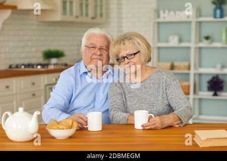 Couples retraités souriants grands-parents assis ensemble dans la cuisine avec thé et biscuits Banque D'Images