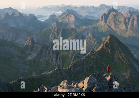 Randonneur sur le sommet rocheux de Hermannsdalstind avec des montagnes de Moskenesøy au loin, îles Lofoten, Norvège Banque D'Images