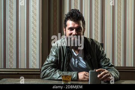 Un homme souriant et charmant qui boit seul. Hippster brutal barbu cognac cher. Problèmes graves de dépendance à l'alcool. Alcoolisme Banque D'Images