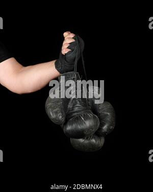 Le bras de l'homme enveloppé dans un bandage élastique noir sports détient old vintage paire de gants de boxe en cuir, fond noir, copy space Banque D'Images