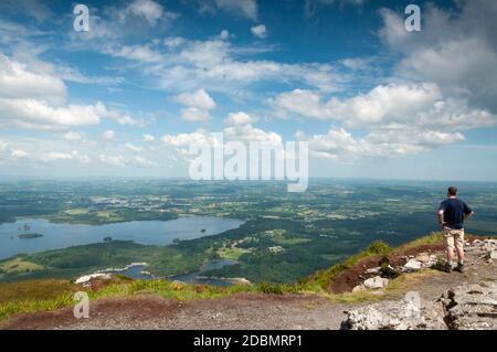 Temps ensoleillé Irlande randonnée en montagne en Irlande paysage pittoresque et pittoresque vue d'ensemble de la vallée de Killarney et des lacs de Killarney et seul randonneur mâle admire la vue depuis le sommet de Torc Mountain par jour ensoleillé dans le comté de Kerry, en Irlande. Banque D'Images