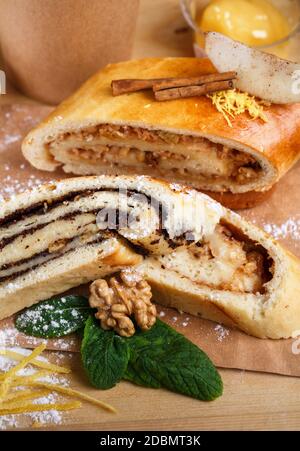 Strudel de pavot et de pomme sur un plateau en bois rustique. Le décor des rouleaux parfumés est composé de cannelle, menthe, noix, zeste de citron et sucre en poudre. Gros plan, flou Banque D'Images