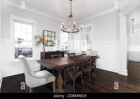 Cette salle à manger luxueuse comprend une table en bois rustique et un lustre en corde/fer suspendu au-dessus de la table. Une cuisine blanche se trouve derrière la salle à manger. Banque D'Images