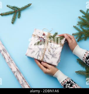 Deux mains tenant un cadeau enveloppé dans du papier d'emballage de fête sur un fond bleu, vue du dessus Banque D'Images