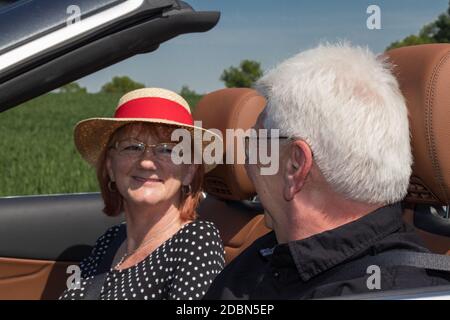 Bon vieux couple conduit avec une voiture de sport de luxe dans la nature par une journée ensoleillée Banque D'Images