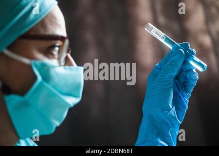 Photographie conceptuelle d'un médecin tenant et regardant un tube à essai tout en testant des échantillons pour la présence de coronavirus (COVID-19). Banque D'Images