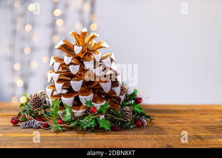 Décoration pomme de pin de Noël. Pomme de pin dorée et blanche ornée de branches de sapin vert et de baies rouges. Banque D'Images