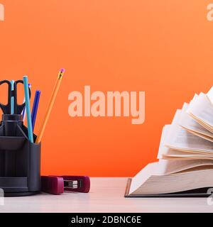 Un livre et un support avec des stylos, des crayons et des ciseaux sur une table en bois clair. Le livre est ouvert, les feuilles de la page sont bronzées, un dos brun orange Banque D'Images