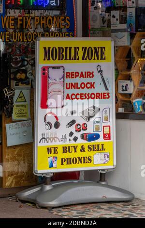 un panneau à l'extérieur d'une boutique offrant le déverrouillage et la réparation de téléphones mobiles ainsi que l'achat et la vente de smartphones et de technologie. Banque D'Images