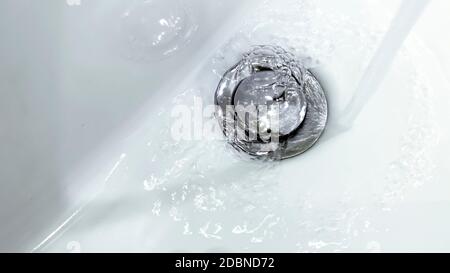 eau tombant d'un robinet dans un évier en céramique blanche avec une crépine métallique Banque D'Images