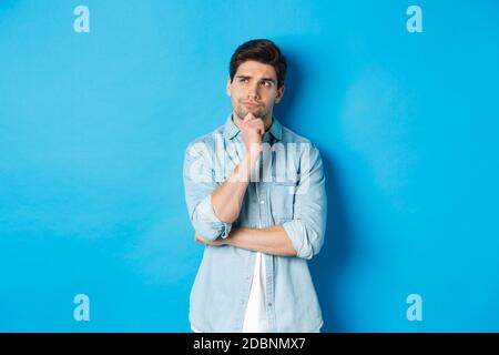 Image d'un homme barbu adulte de 25 ans, en pensant à quelque chose, en regardant dans le coin supérieur gauche et en réfléchissant des idées, debout sur fond bleu Banque D'Images