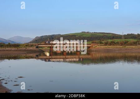 Un train de sprinters Northern Rail traverse la rivière Mite à Ravenglass sur la ligne de chemin de fer de la côte de Cumbrian se reflète dans le rivière en contrebas Banque D'Images