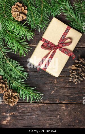 Boîte cadeau enveloppée de papier artisanal, de branches et de cônes de pin sur fond de bois rustique foncé. Vue de dessus avec espace de copie pour votre texte. Vacances d'hiver con Banque D'Images