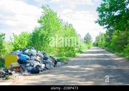 Décharge illégale près de la route de sable de pays dans le pays le jour de soleil. Corbeille de la pollution dans la nature. Dirty dépotoir près de bois de la forêt Banque D'Images