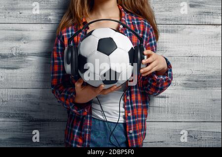 Une petite fille met un casque sur le ballon en studio. Enfants et gadgets, enfant isolé sur fond de bois, émotion de l'enfant, session de photo d'écolière Banque D'Images